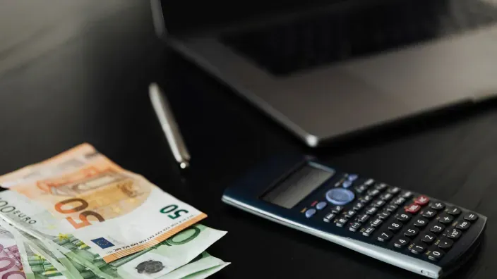 Billetes de euro junto a una calculadora y un portátil para gestionar gastos o finanzas.