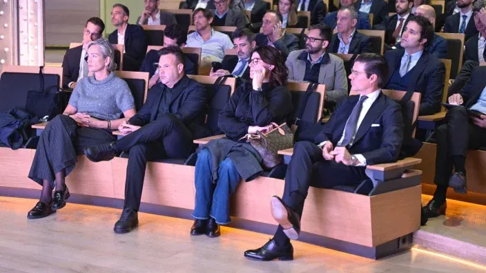 Público asistente sentado en un auditorio durante un evento corporativo, con varias personas observando la presentación.