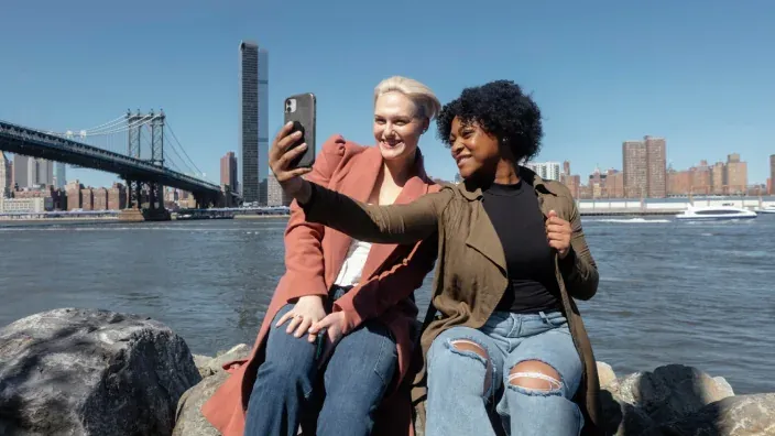 Amigas haciéndose un selfie con smartphone frente al puente de Brooklyn en Nueva York.