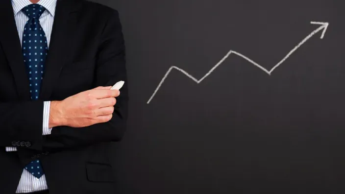 Empresario con tiza junto a un gráfico de crecimiento ascendente.