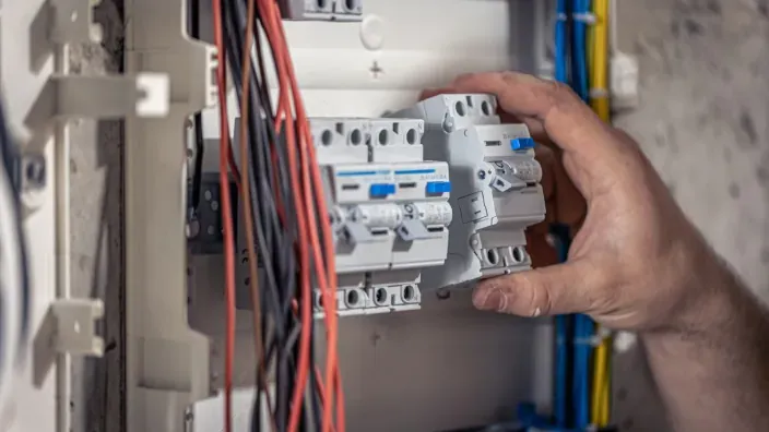 Mano ajustando interruptores automáticos en un cuadro eléctrico con cableado visible.