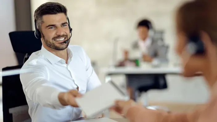 Agente de atención al cliente con auriculares entrega un producto o documento a una clienta.