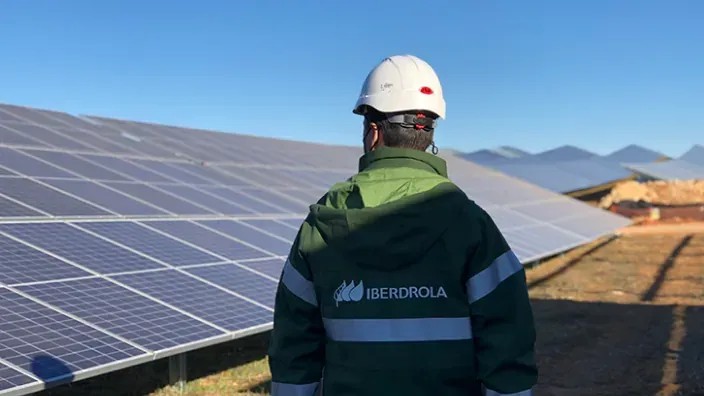 Técnico de Iberdrola inspeccionando paneles solares con uniforme y casco de seguridad.