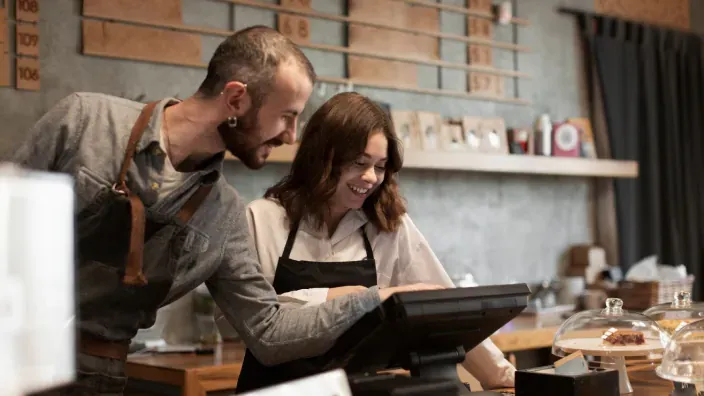 Empleados de hostelería gestionando pedidos en pantalla de TPV táctil en cafetería.