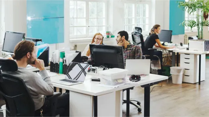 Empleados trabajando en una oficina moderna y luminosa con ordenadores portátiles y áreas de coworking.