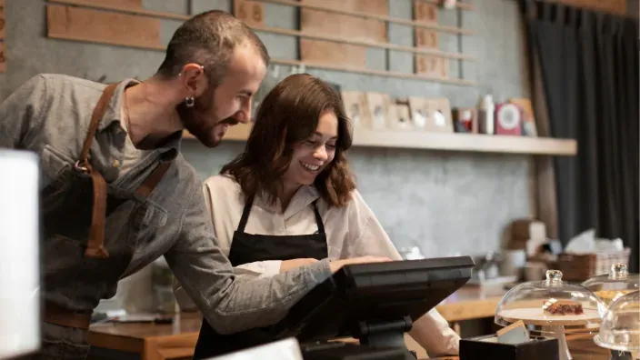 Dos personas sonrientes trabajando juntas en la caja de un pequeño negocio.