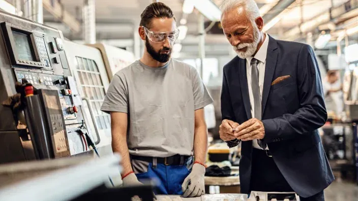 Empresario senior asesora a un trabajador en una fábrica industrial durante un proceso de producción.