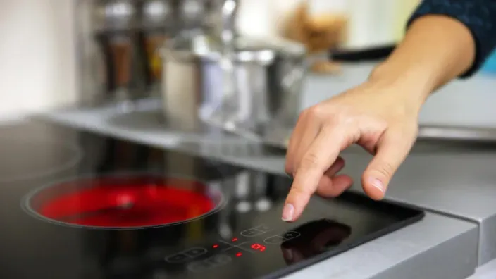 Mano encendiendo una placa de induccion electrica en una cocina moderna
