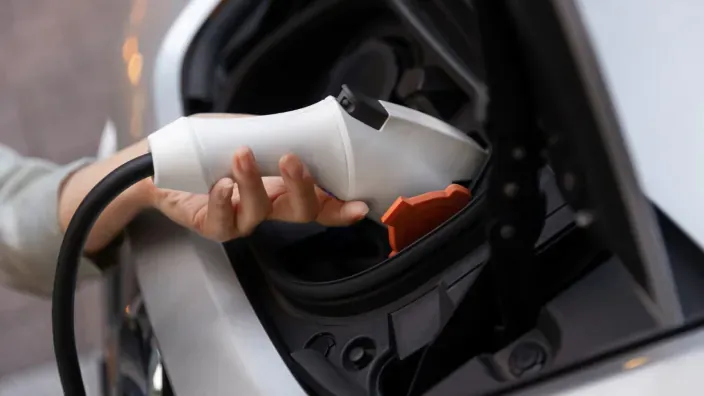 Mano conectando el cable de carga a un coche eléctrico durante el proceso de recarga.