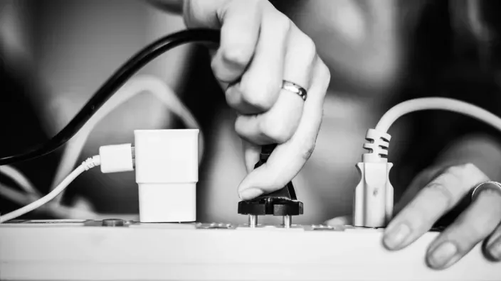 Primer plano de una persona enchufando un cable eléctrico en una regleta, en blanco y negro, relacionado con el ahorro energético.