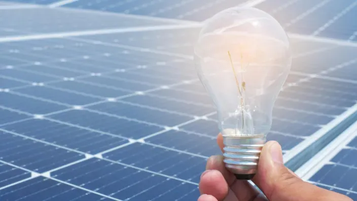 Bombilla sostenida frente a paneles solares como símbolo de energía renovable
