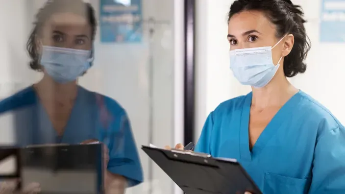 Enfermera con mascarilla y uniforme azul revisando un historial médico en una clín