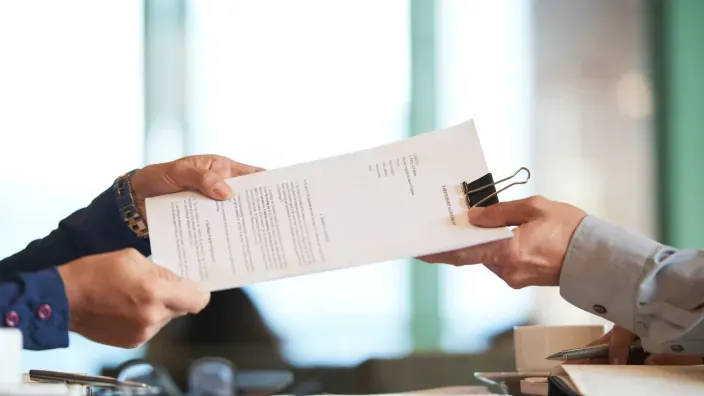 Primer plano de dos manos intercambiando un contrato o documento legal.