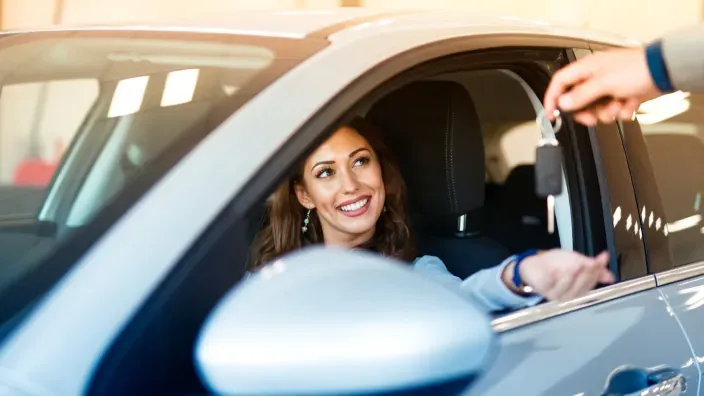 Mujer sonriendo desde el interior de un coche mientras recibe las llaves del vehículo.