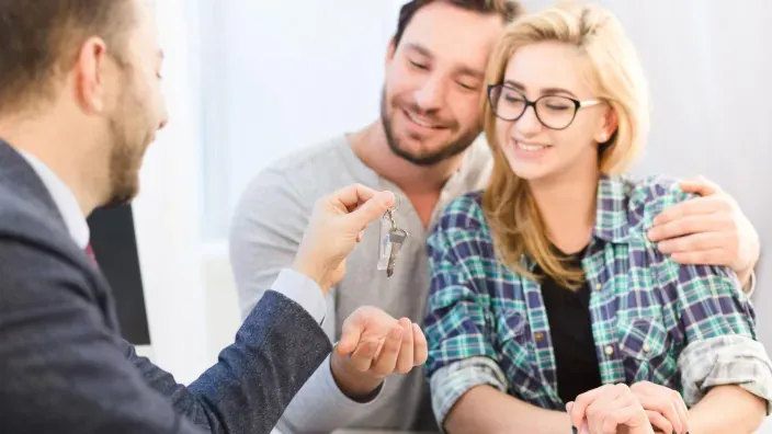 Pareja feliz recibiendo las llaves de su nueva casa de un agente.