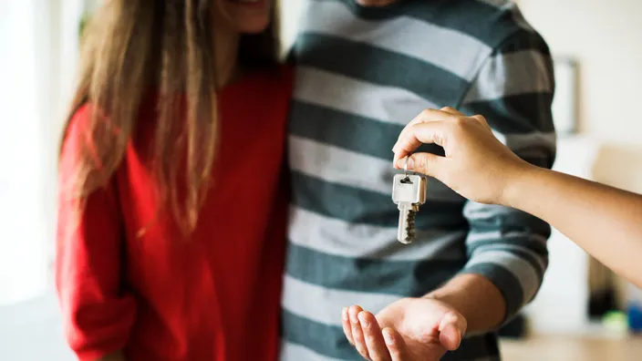 Pareja joven recibe las llaves de su nuevo piso o casa. Concepto de compra, alquiler o firma de una hipoteca con una inmobiliaria.
