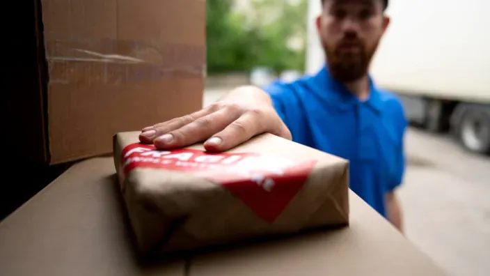 Primer plano de repartidor colocando paquete posible estafa brushing sobre otros paquetes en camión.