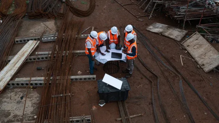 Equipo de obreros con casco revisando planos en una obra desde una vista cenital