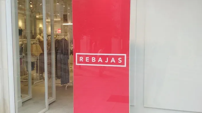 Cartel de “Rebajas” en un escaparate de tienda, con el interior de la tienda visible al fondo.