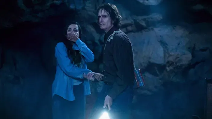 Los personajes de From Victor y Tabitha dentro de una cueva con una linterna encendida