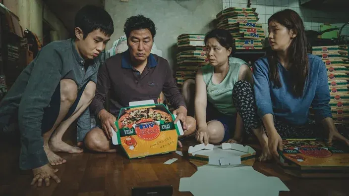 Escena de la familia Kim doblando cajas de pizza en la película coreana Parásitos.
