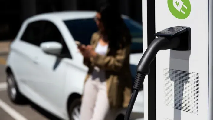 Estación de recarga de coche eléctrico con una persona usando el móvil