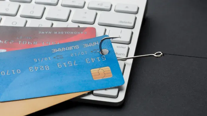 Tarjeta de crédito enganchada por un anzuelo sobre un teclado de ordenador, representando un intento de phishing financiero.