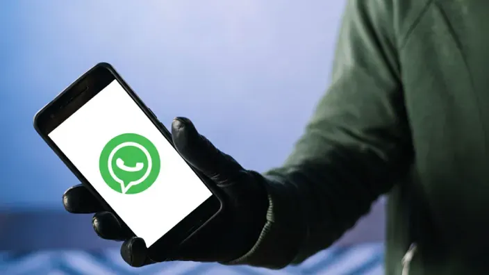 Persona con guantes sosteniendo un teléfono móvil con el logotipo de WhatsApp en la pantalla, representando una posible estafa digital.