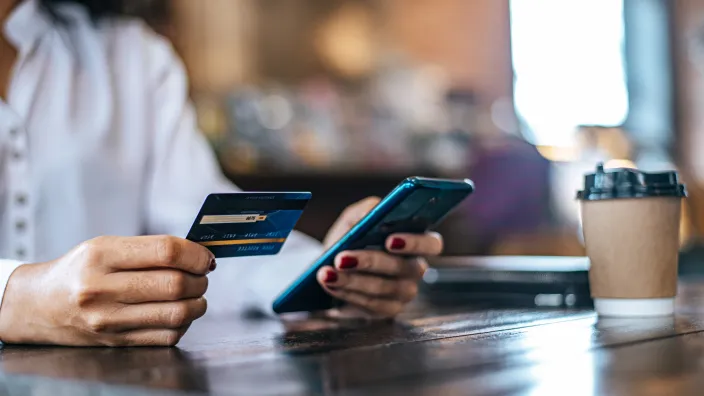 Mujer realizando un pago online con su tarjeta de crédito y su smartphone en una cafetería.