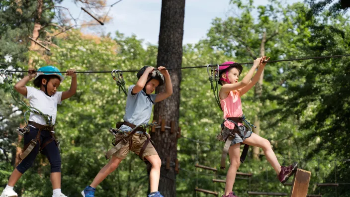 Niños equipados con casco y arnés en un parque de aventura, una actividad de campamento de verano en los árboles.