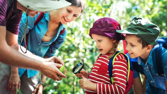 Monitores de campamento enseñando a niños a explorar la naturaleza con una lupa en una excursión por el bosque.