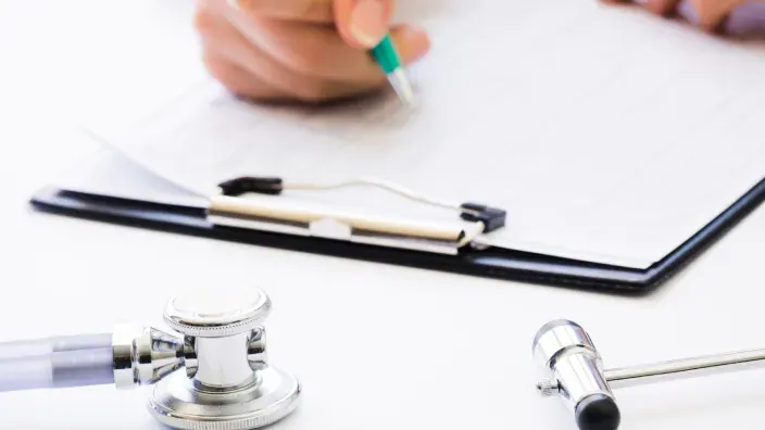 Estetoscopio y documentos médicos sobre una mesa con una persona escribiendo al fondo