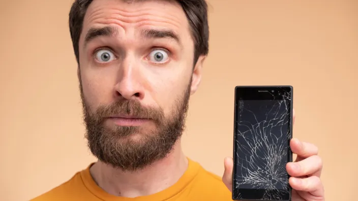 Hombre con cara de sorpresa mostrando su smartphone con la pantalla completamente rota, un accidente cubierto por el seguro.