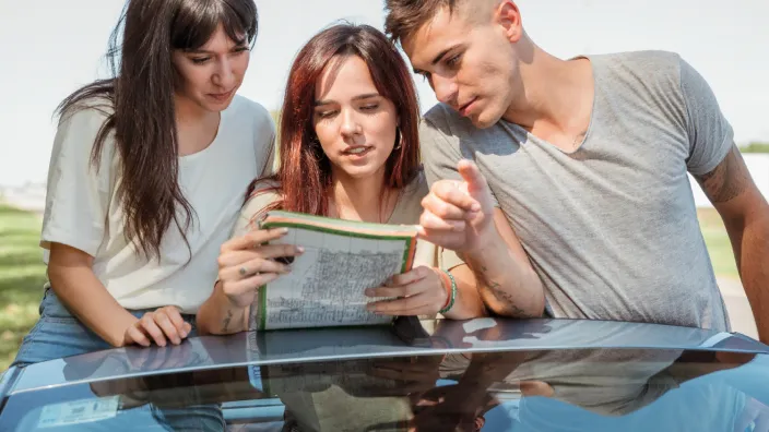 Grupo de amigos mirando un mapa sobre el capó de un coche, planificando su ruta durante un viaje por carretera.