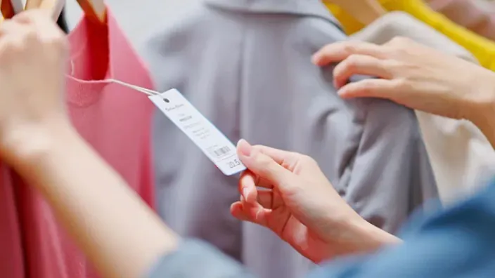 Clienta revisando el precio en la etiqueta de una prenda de ropa rosa en tienda de moda.