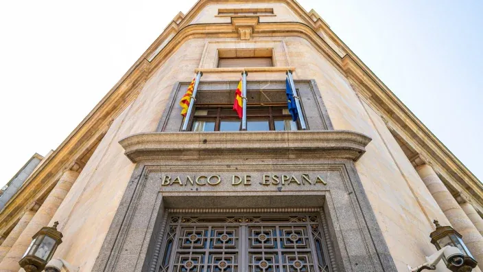 Fachada del Banco de España con banderas y arquitectura clásica vista desde un ángulo inferior.