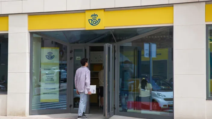Una persona entrando en una oficina de Correos para realizar una gestión o contratar un servicio.