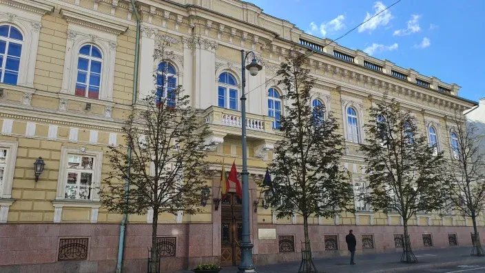 Fachada principal del Banco de Lituania con banderas en la entrada y árboles frente al edificio