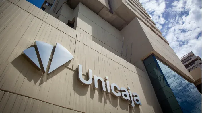 Vista en contrapicado de la fachada de un edificio de Unicaja, destacando el logotipo y las letras corpóreas metálicas de la marca bajo el cielo azul