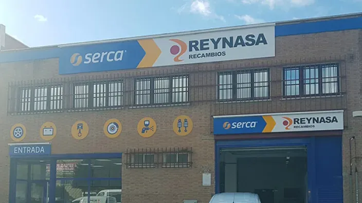 Fachada de la tienda Reynasa Recambios y Serca con iconos de repuestos de coche y mantenimiento automotriz.
