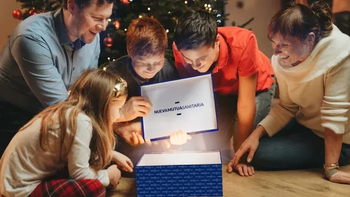 Familia reunida alrededor de una caja abierta con el logotipo de Nueva Mutua Sanitaria