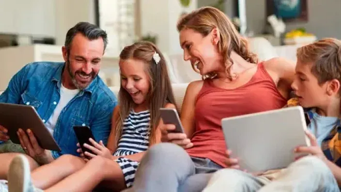 Familia conectada en el hogar usando tablets y móviles en el sofá, simbolizando el ocio y la tecnología digital.
