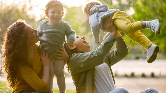 Familia con dos hijos pequeños jugando y riendo juntos en un parque al aire libre.