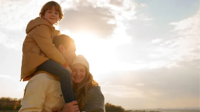Familia feliz abrazándose al aire libre bajo la luz del sol, simbolizando protección y bienestar.