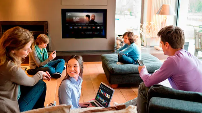 Familia reunida en el salón viendo la televisión y usando portátil con contenidos de Movistar Plus+.