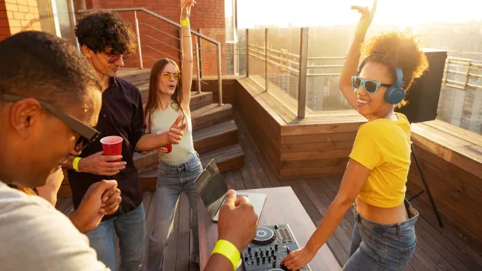 Grupo de jóvenes amigos en una fiesta en una azotea con un DJ al atardecer.