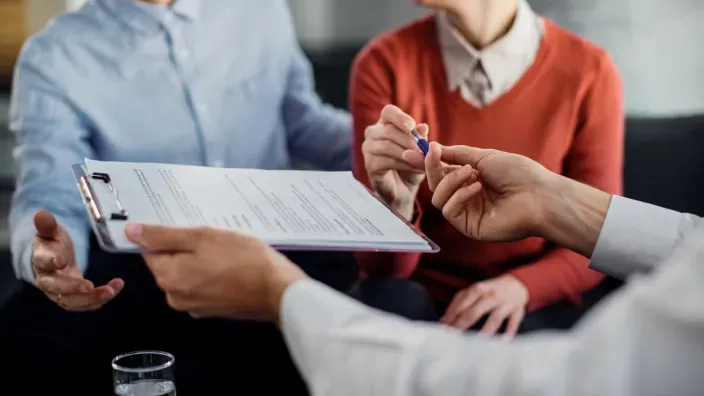 Asesor financiero ofrece un bolígrafo a una pareja para firmar un contrato de seguro o hipoteca.