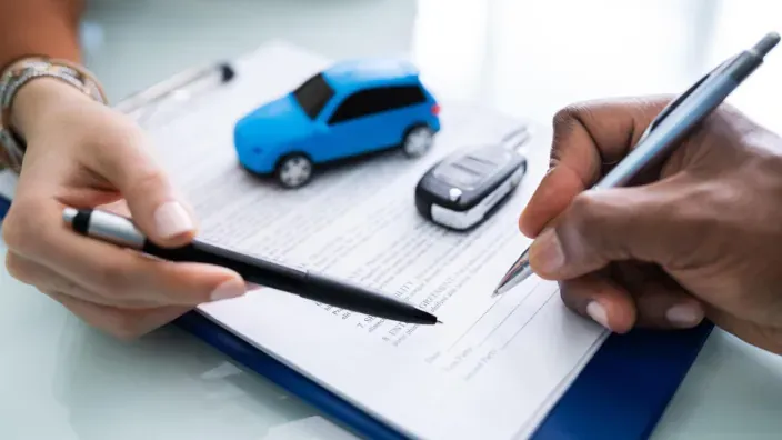 Firma de un contrato de seguro de coche con llaves y una maqueta de auto azul sobre un escritorio.