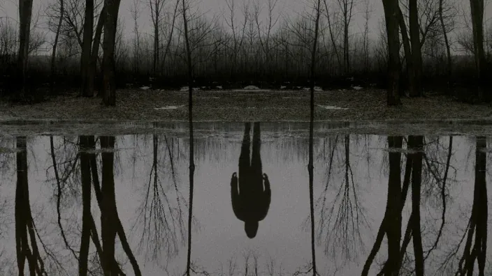 Imagen promocional de El Visitante, con un reflejo en el agua en un ambiente oscuro.