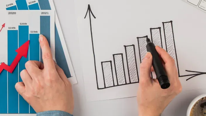 Persona dibujando a mano gráfico de crecimiento financiero y comparándolo con datos impresos.